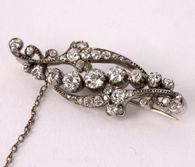 Lot 100 - A diamond brooch of scrolling form, the...